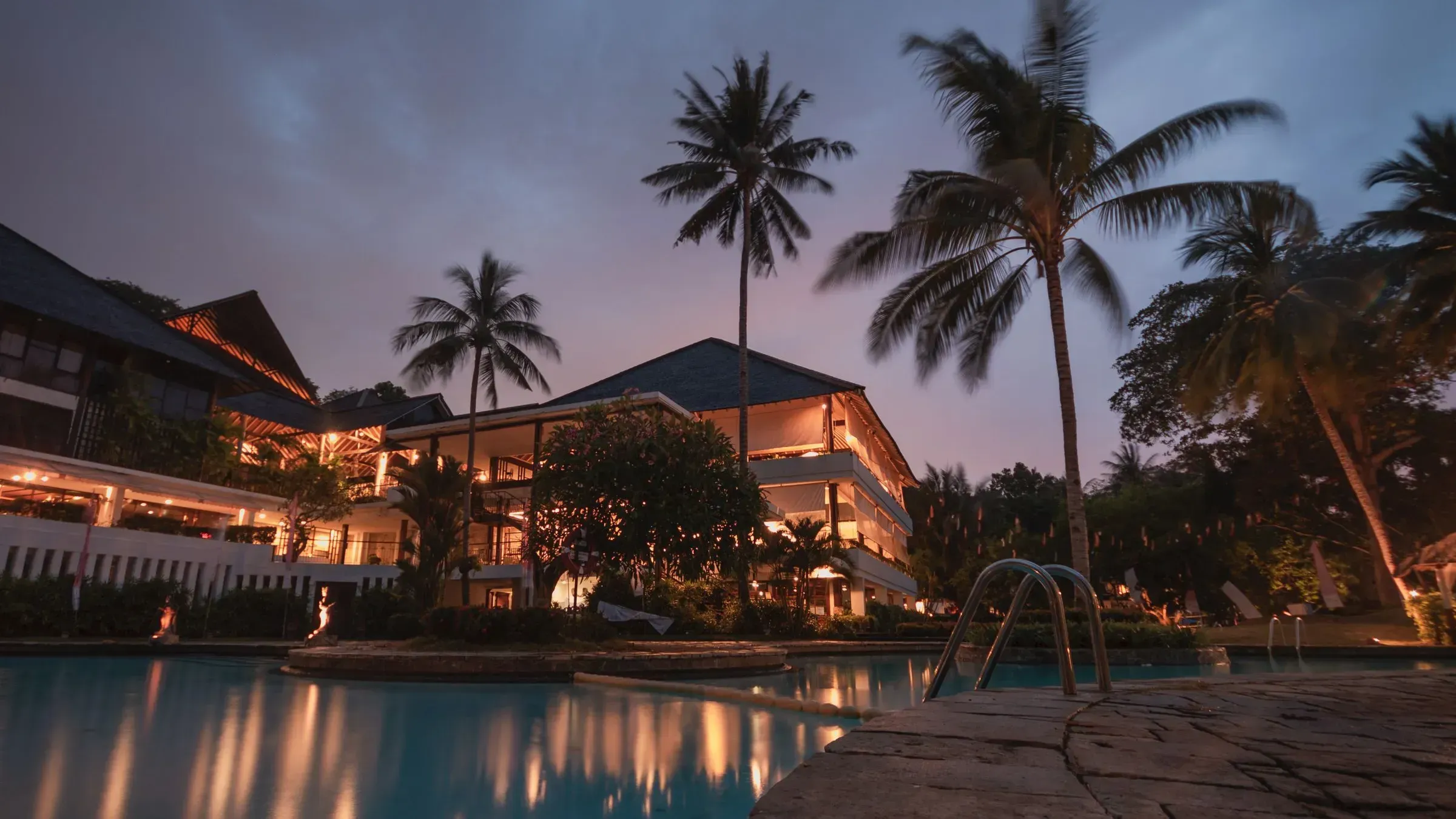 Hotel junto a la piscina al anochecer, rodeado de palmeras